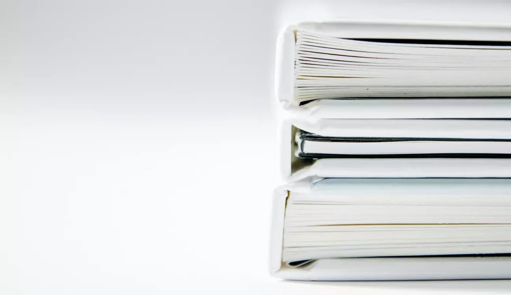 Stos oprawionych dokumentów projektowych na jasnym tle, ilustrujący gotową dokumentację briefu projektowego. Zdjęcie towarzyszy artykułowi „Co to jest brief i co powinien zawierać? Poznaj 9 niezbędnych elementów tego dokumentu” na blogu Akademii Projektowania i Kursu Projektowania Graficznego, Weronika Wolska